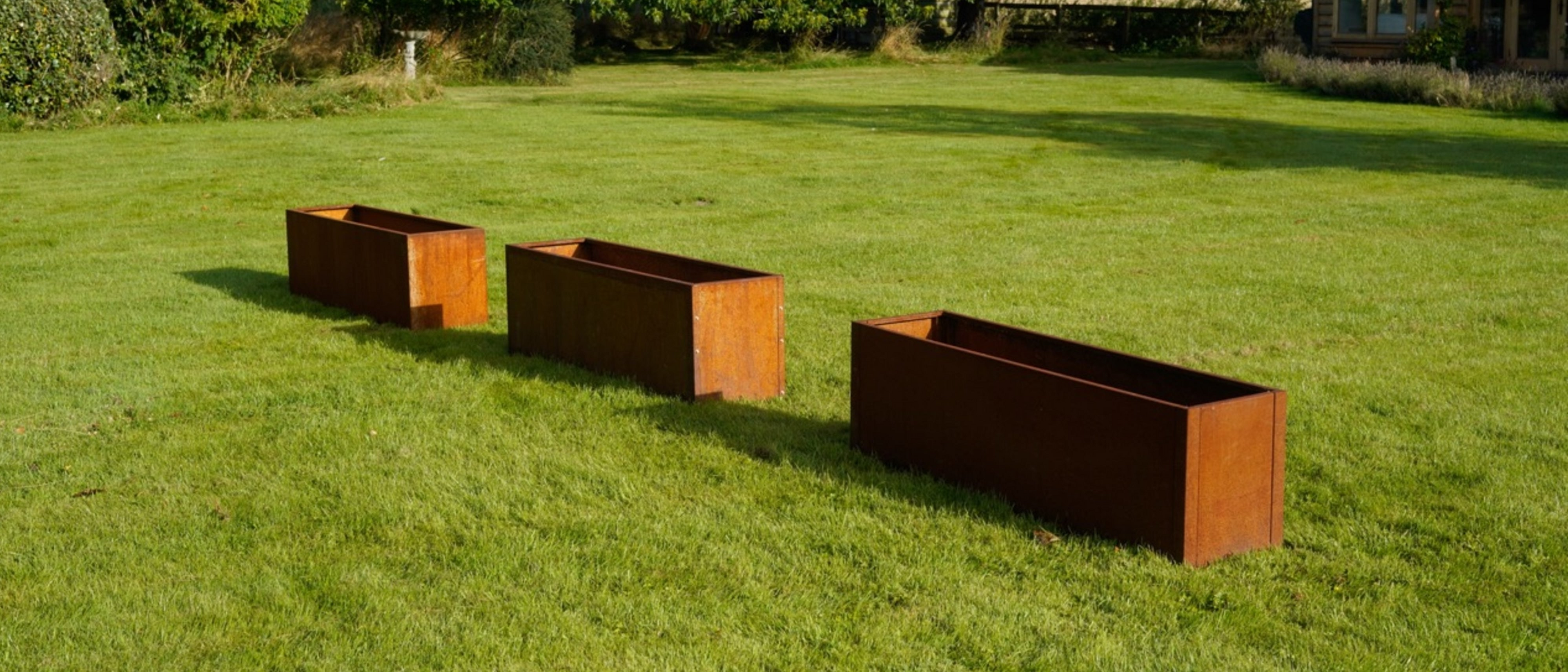 Three externally fixed Corten steel planters in a grass garden