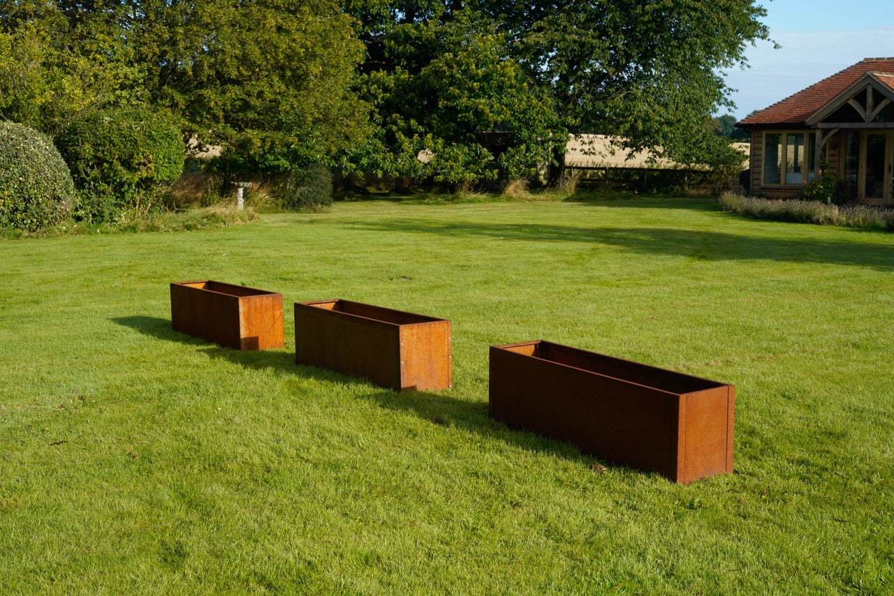 Three externally fixed Corten steel planters in a grass garden